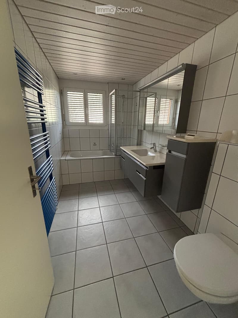 Modern bathroom with tiled walls and floor, featuring a sink with a mirror, a toilet, a bathtub, and a glass-enclosed shower area.