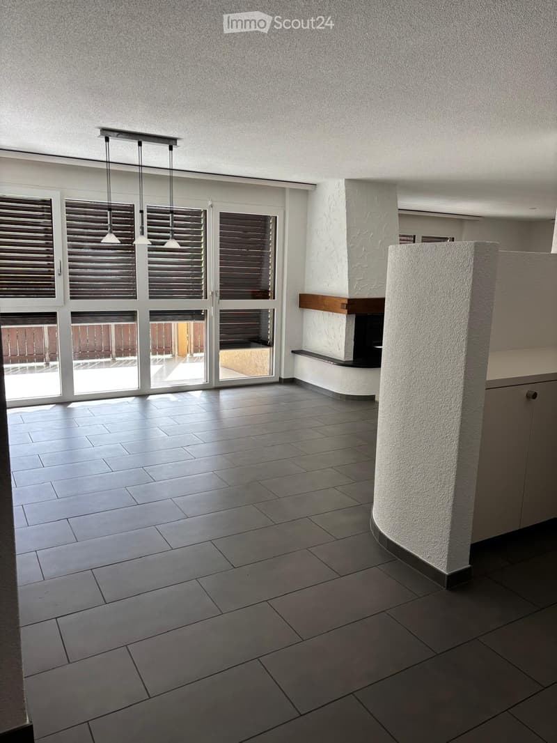 Empty room with tiled floor, large windows with blinds, and a fireplace area with a wooden mantle.