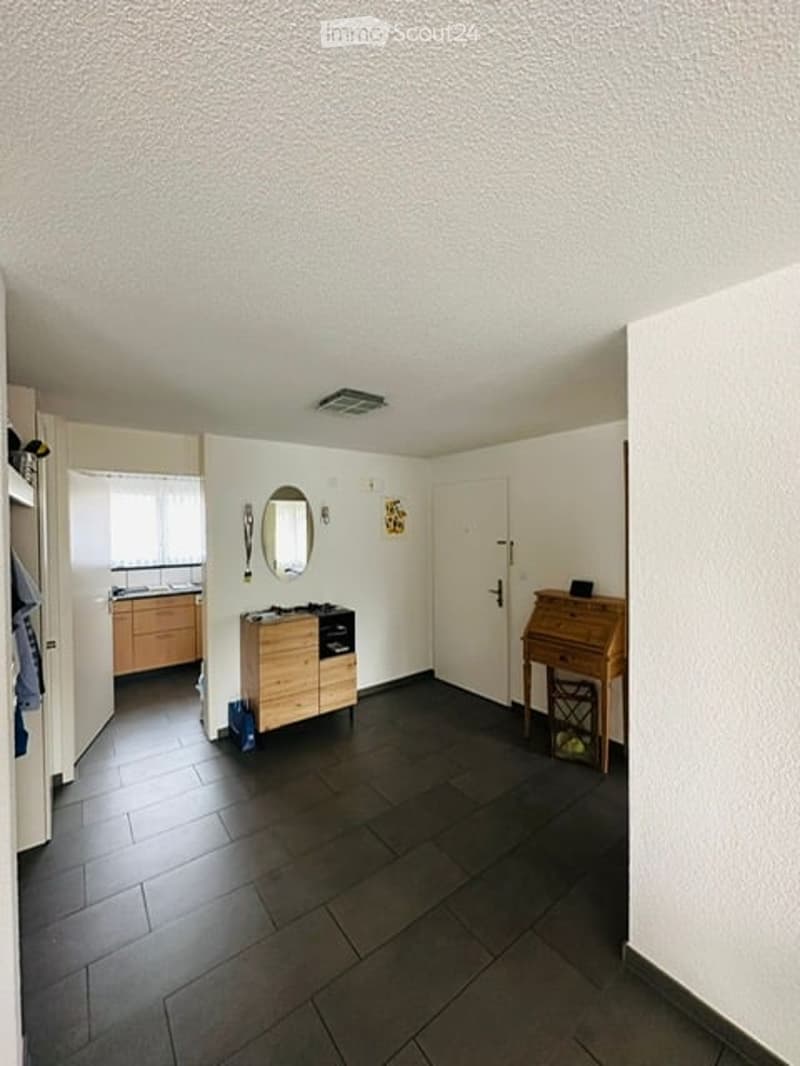 Empty room with white walls, black tiled floor, wooden cabinet, mirror, and a desk.