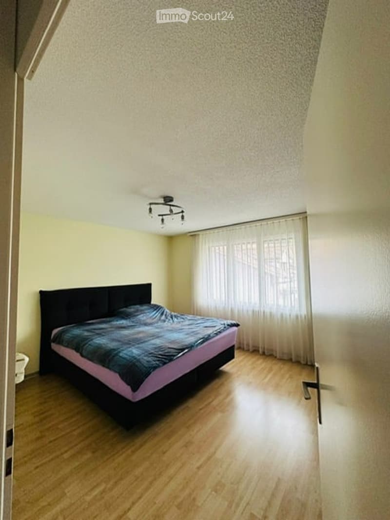 Bedroom with bed, yellow walls, wooden floor, white curtains, ceiling lamp