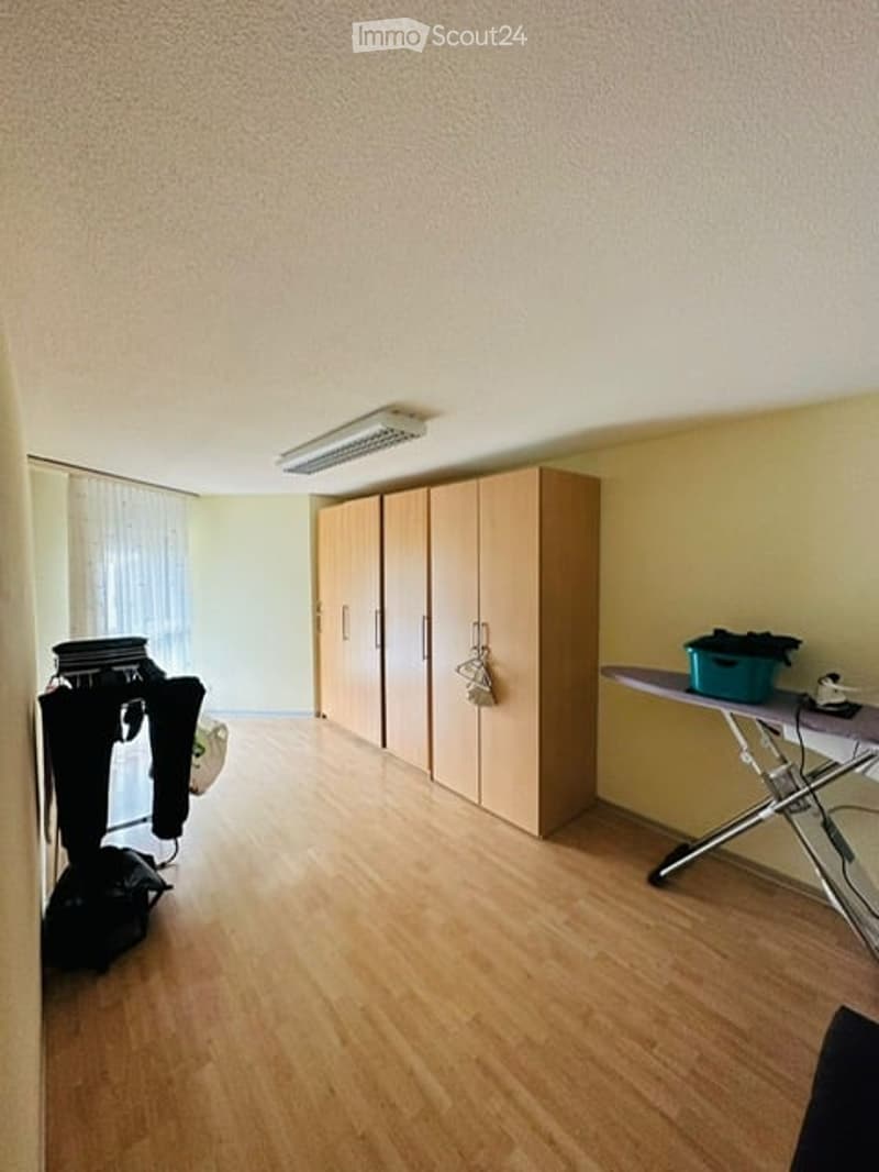 Empty room with wooden floor, three wooden cabinets, an ironing board, and a white curtain