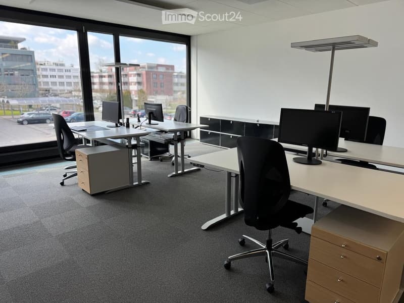modern office with large windows, desks, chairs, monitors, cabinets, carpeted floor
