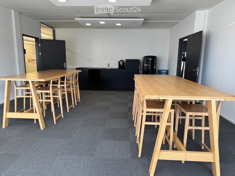 empty room with two long wooden tables, wooden chairs, black kitchen cabinets, black refrigerator, black coffee machine, sink, faucet