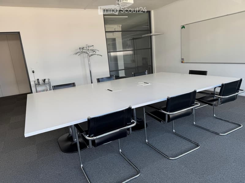 A conference room with a long white table, black chairs, a whiteboard, and a projector.