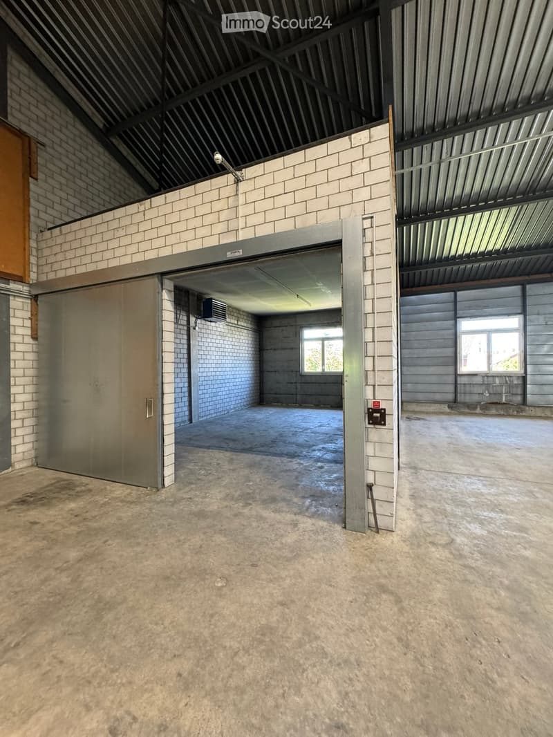 Empty industrial-style room with concrete floor, brick walls, metal ceiling, and large garage door. No furniture or equipment present.