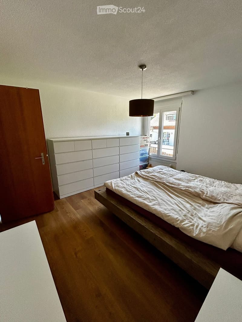 Bedroom with wooden floor, white walls, large bed, white dresser, window with view