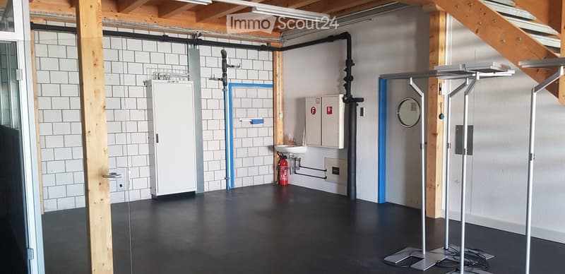 Empty room with white tiled walls, wooden beams, black floor, white door, sink, fire extinguisher, metal stands