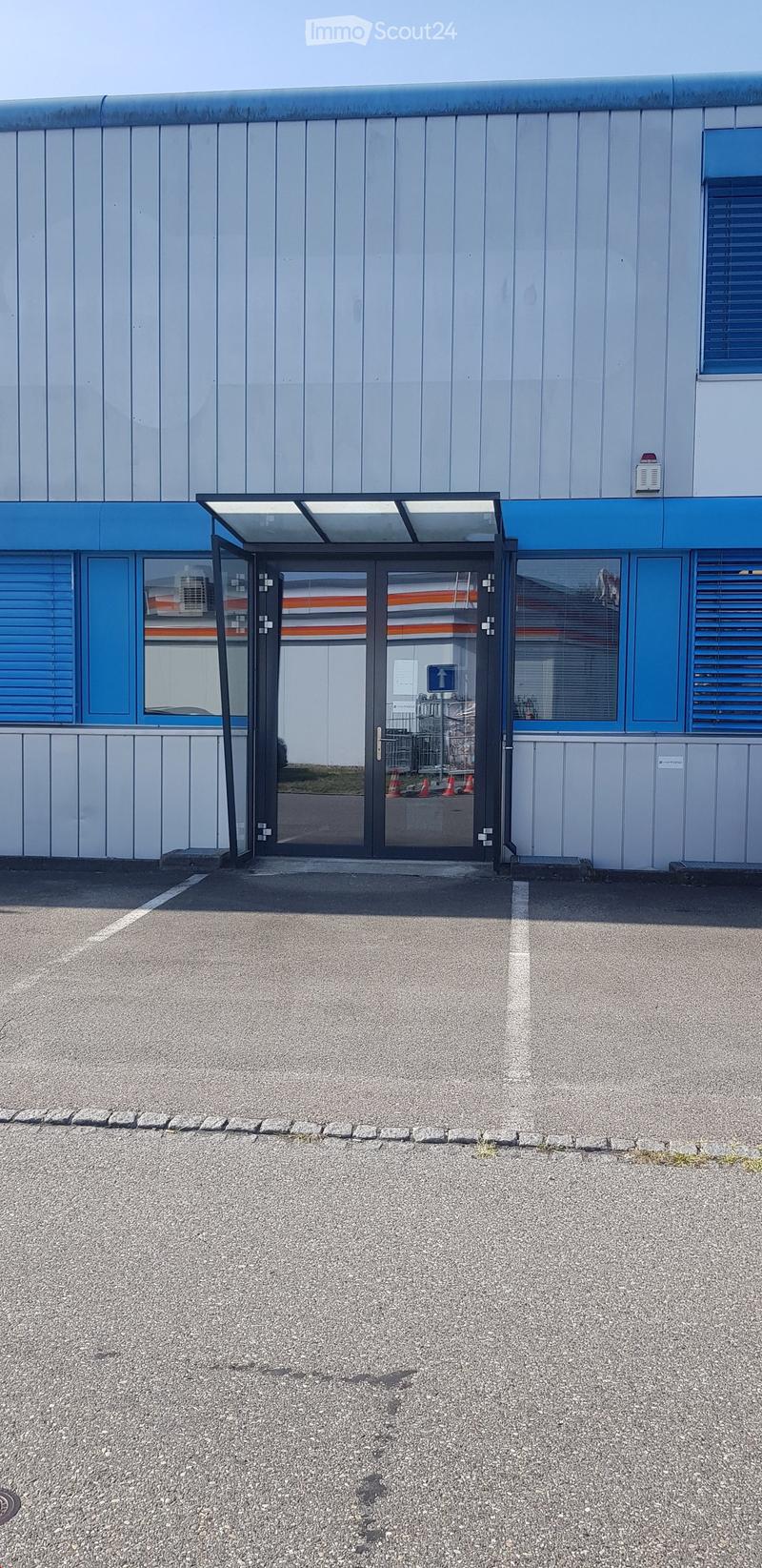 Commercial building with blue walls, white panels, glass doors, and windows, with a parking area in front.