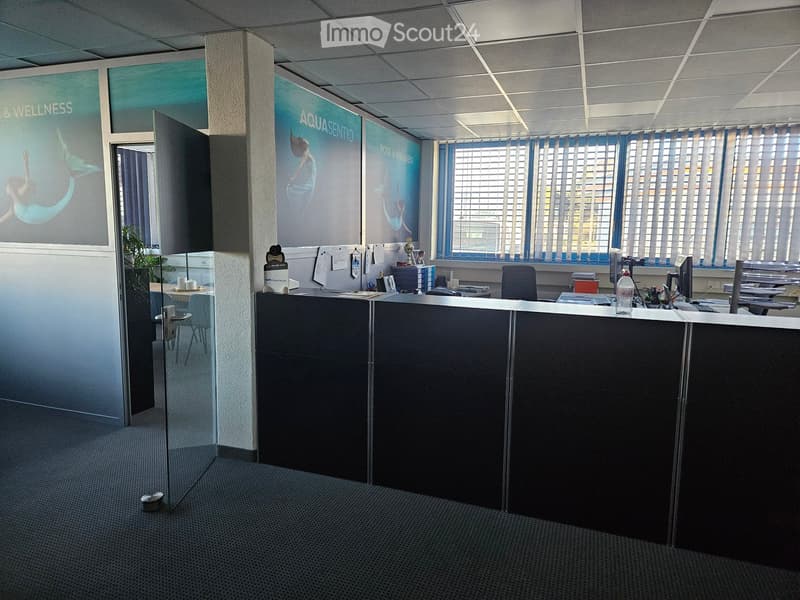 Empty office with a reception desk, chairs, computer monitors, and a window with blinds.