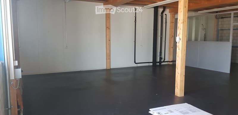 Empty room with white walls, wooden beams, black floor, pipes, and electrical outlets.