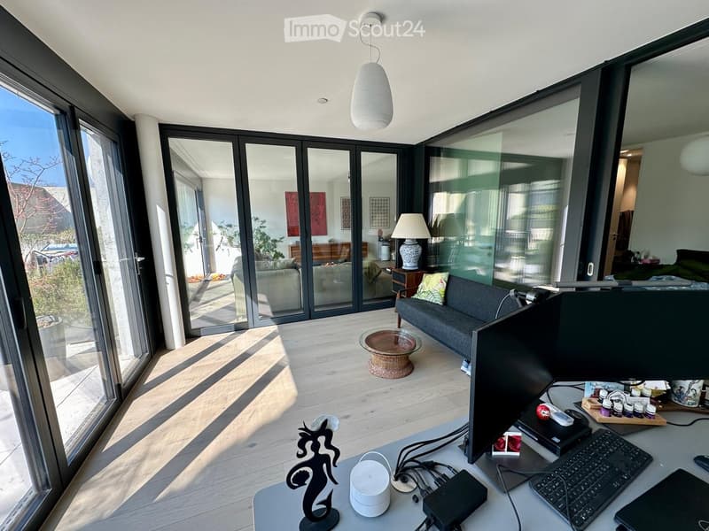 modern living room with sliding glass doors, hardwood floors, large windows, desk with computer, couch, coffee table, lamp, and decorative items