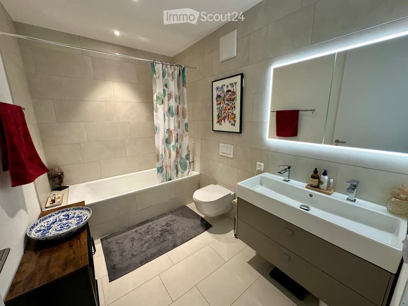 Bathroom with bathtub, toilet, double sink, mirror, towel rack, and tiled floor