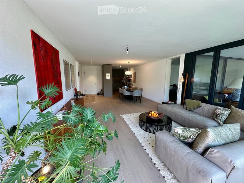 modern living room with wooden floor, gray sofas, round coffee table, large windows, dining table, and artwork