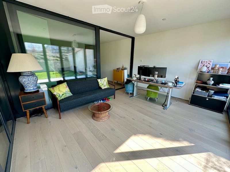 modern living room with large windows, hardwood floors, couch, desk, lamp, shelves, and a view of the outside