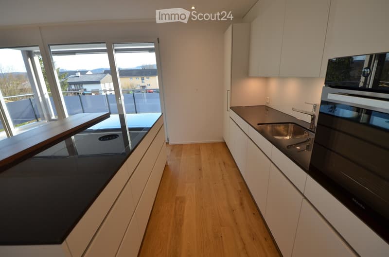 modern kitchen with wooden floor, white cabinets, black countertops, large windows, stainless steel sink, faucet, oven