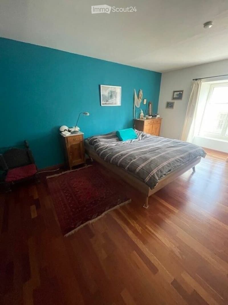 bedroom with wooden floor, blue wall, bed, nightstand, lamp, rug, chair, cabinet, picture frames