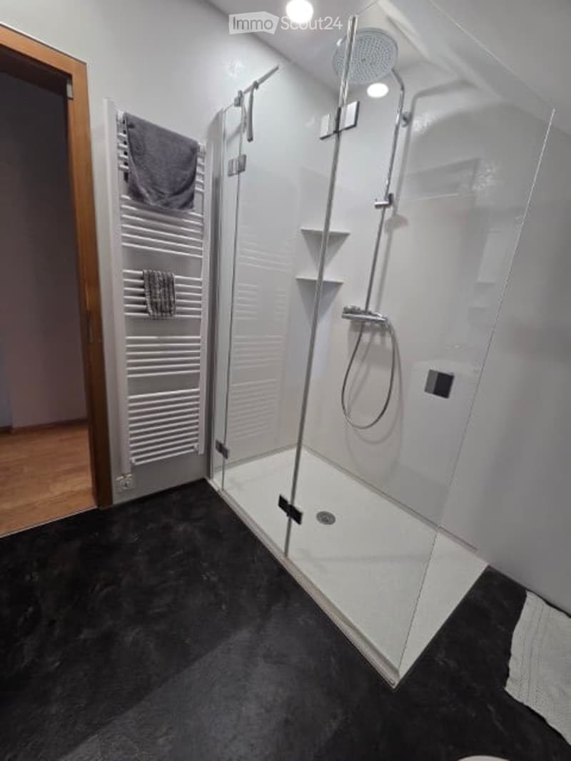 Modern bathroom with glass shower enclosure, white tiles, black floor, white towel rack, and a towel hanging on it
