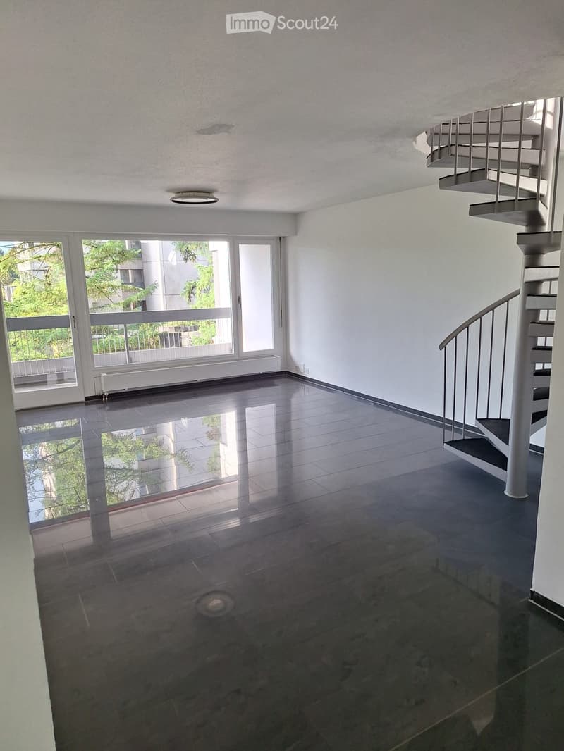 Empty room with white walls, black tiled floor, spiral staircase, and large windows with railings.