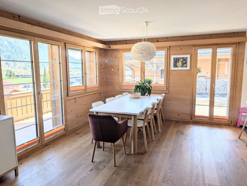Dining room with wooden walls, large windows, wooden floor, white table, chairs, and a plant
