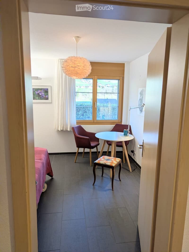 small room with a bed, a table, two chairs, a lamp, and a window with a view