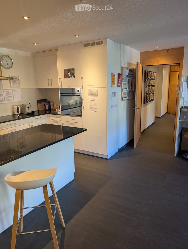 modern kitchen with white cabinets, black granite countertops, wooden stool, built-in oven and microwave, clock, and refrigerator