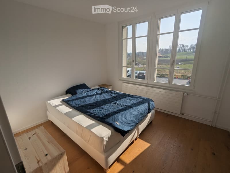 Bedroom with bed, wooden floor, white walls, large windows, view of the outside