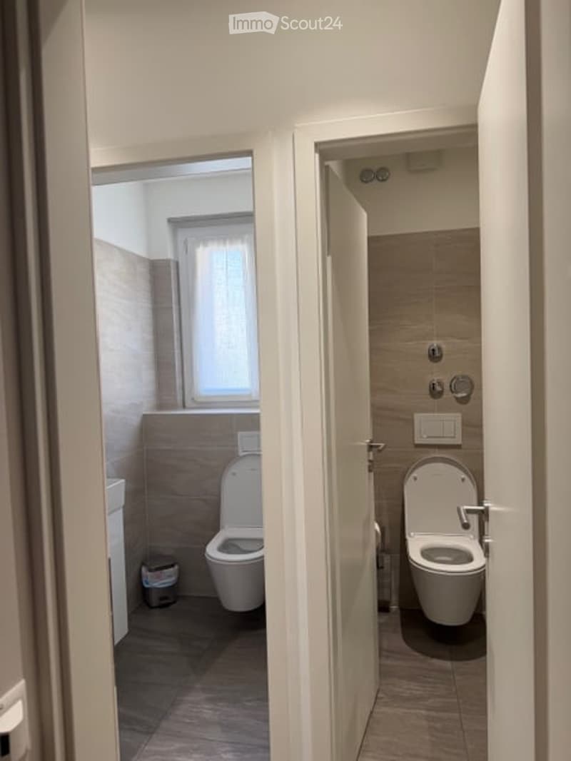 Bathroom with two toilets, sink, window, tiled floor, and wall