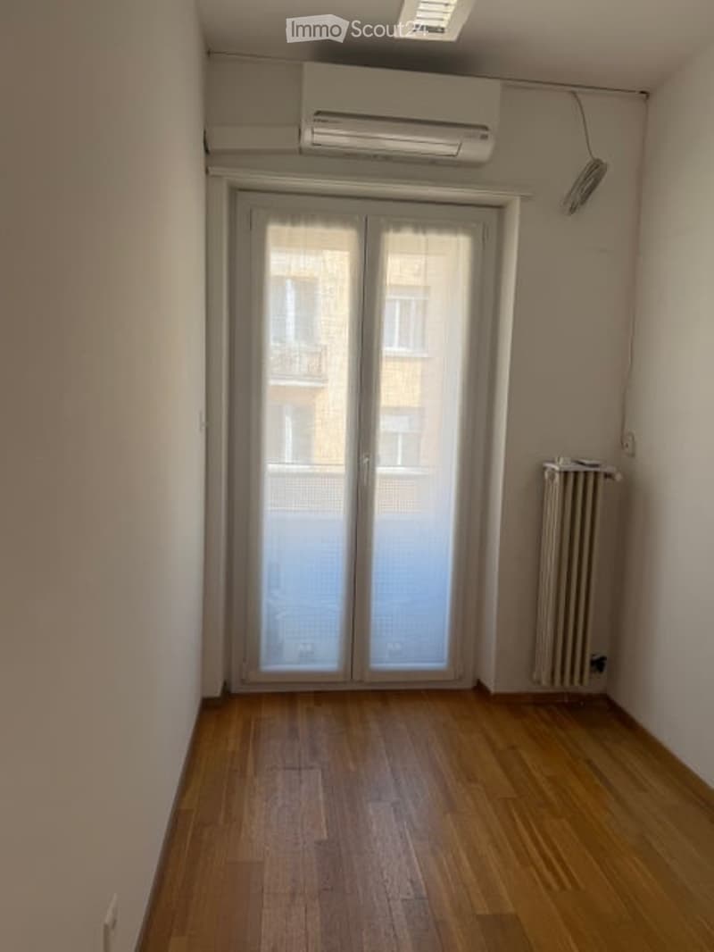 Empty room with wooden floor, white walls, sliding glass doors, air conditioner, and radiator