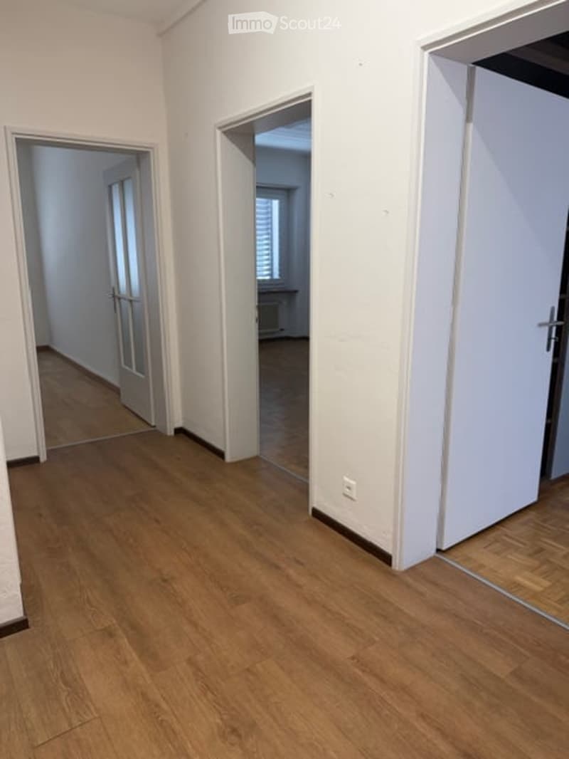 Empty room with wooden floor, white walls, three doors, power outlet