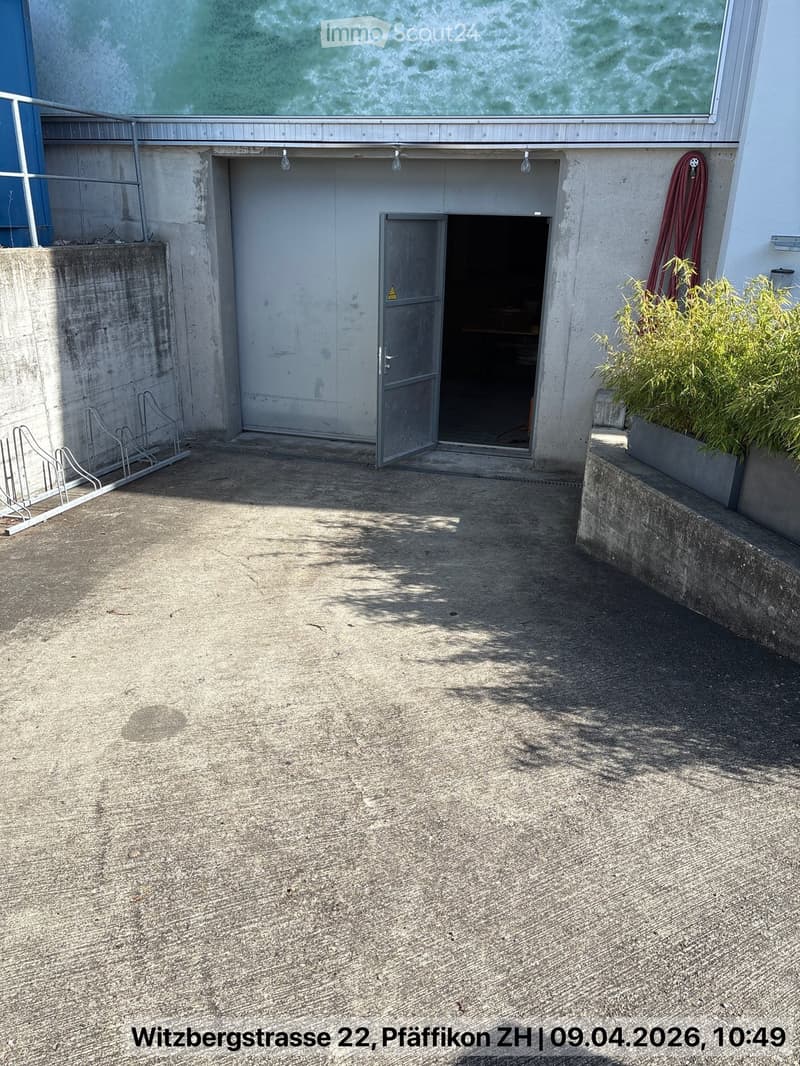 Concrete building with an open garage door, a bicycle rack, and a small plant on the right side.