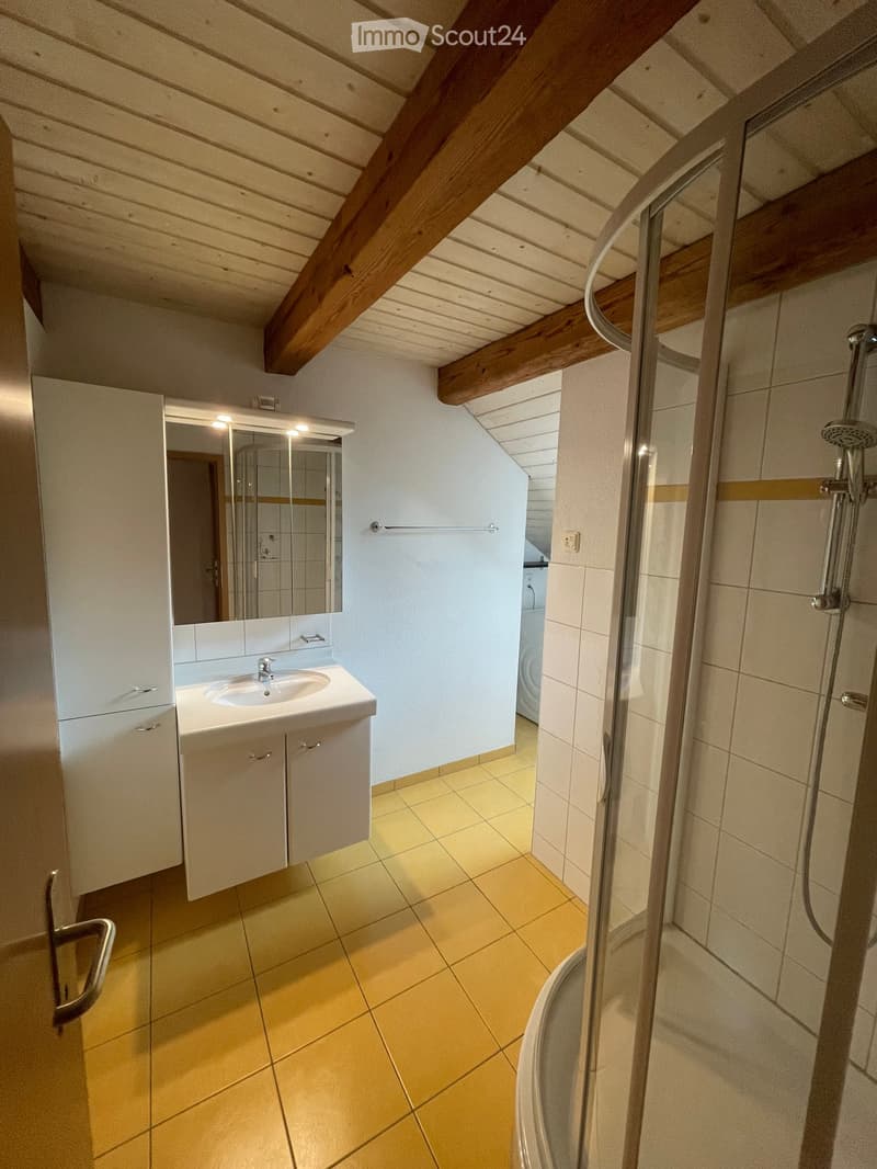 Bathroom with yellow tiles, white sink, mirror, shower, and wooden beams on the ceiling.
