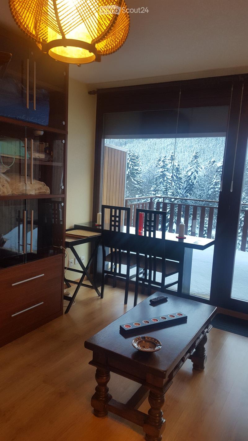living room with wooden floor, large windows, balcony, table, chairs, cabinet, remote control, plate, candle holder