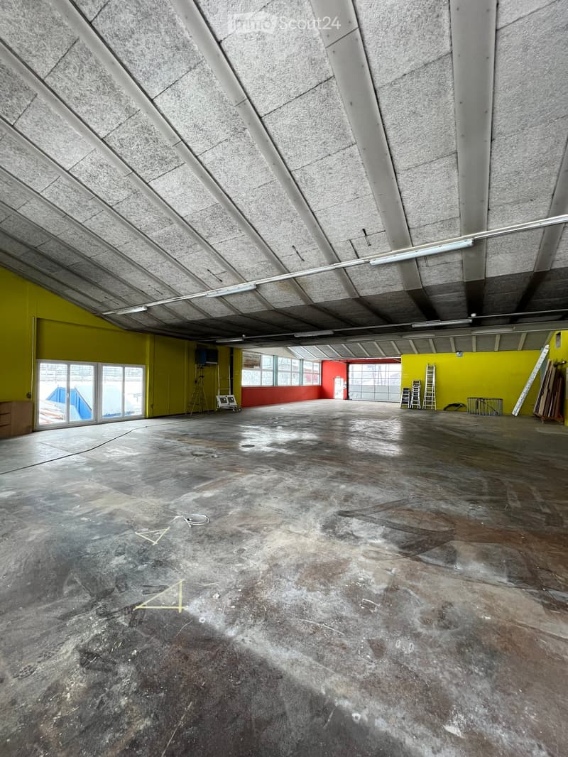 Empty room, concrete floor, yellow and red walls, large windows, ladders, equipment