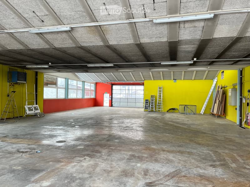 Empty room with concrete floor, yellow and red walls, large windows, ladders, and storage items