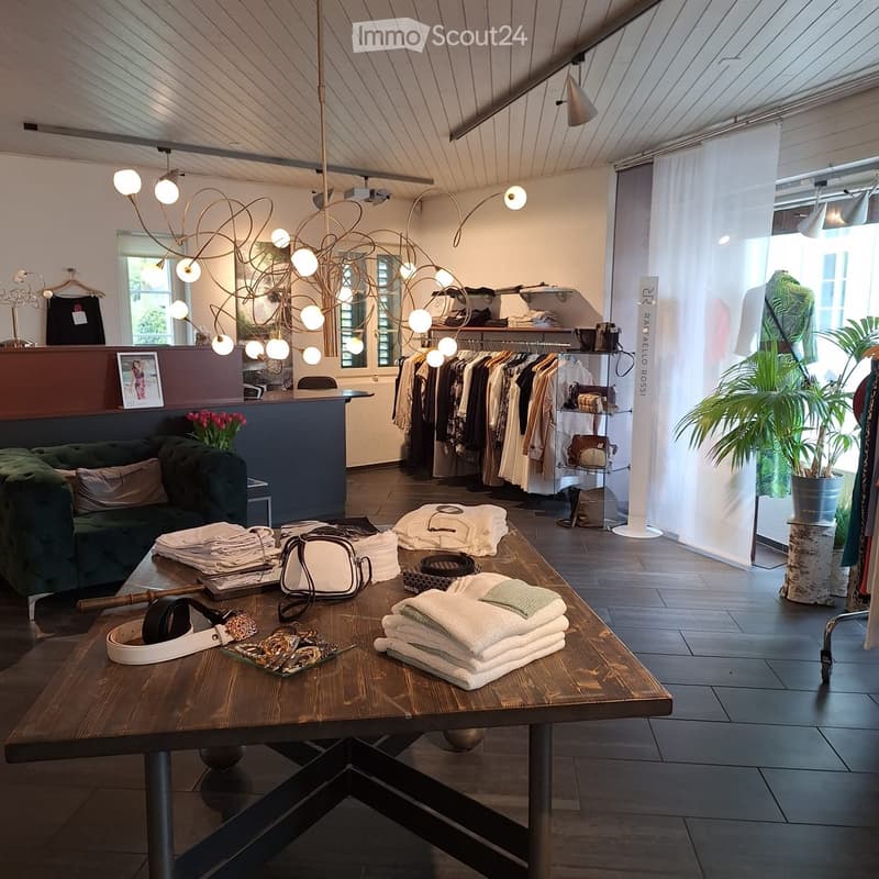 A clothing store with a wooden table, green couch, clothes on hangers, and a chandelier.