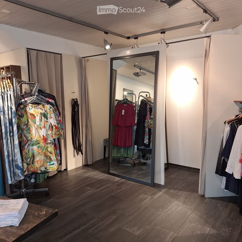 Clothing store with clothes on racks, large mirror, wooden floor, track lighting