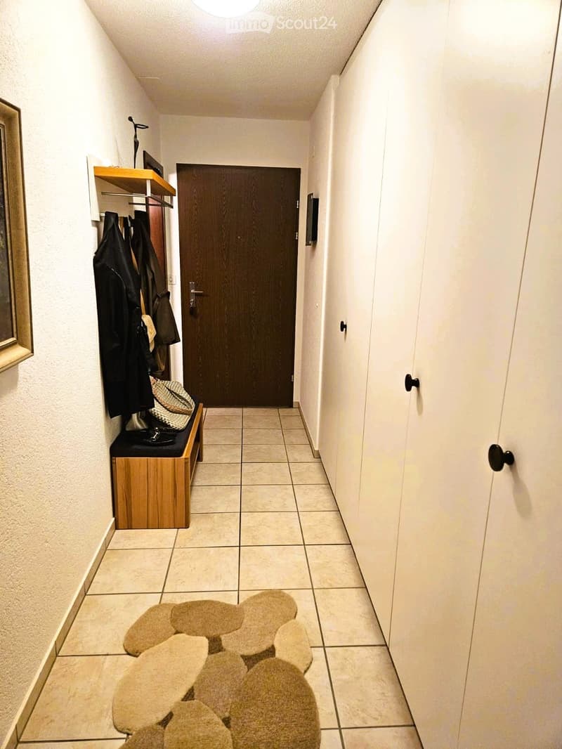tiled floor, wooden bench, coat rack, white walls, wooden door, closets