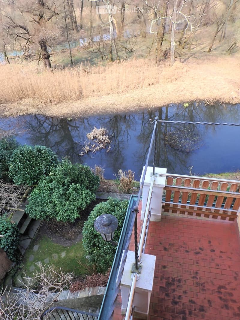 Balcony with railings, brick floor, lamp, shrubs, and a view of a river