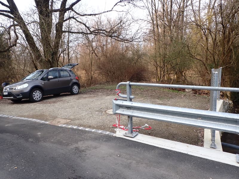 Car parked on gravel, metal barrier, trees, road
