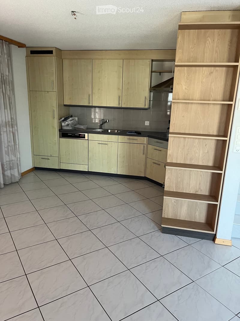 Modern kitchen with light wooden cabinets, a sink, a dishwasher, and open shelving units. The floor is tiled with large, light-colored tiles.