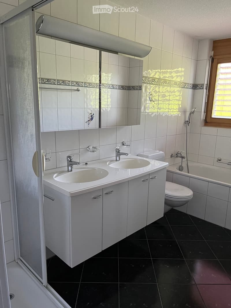 Modern bathroom with white tiles, double sink, mirror, toilet, bathtub, and shower area.