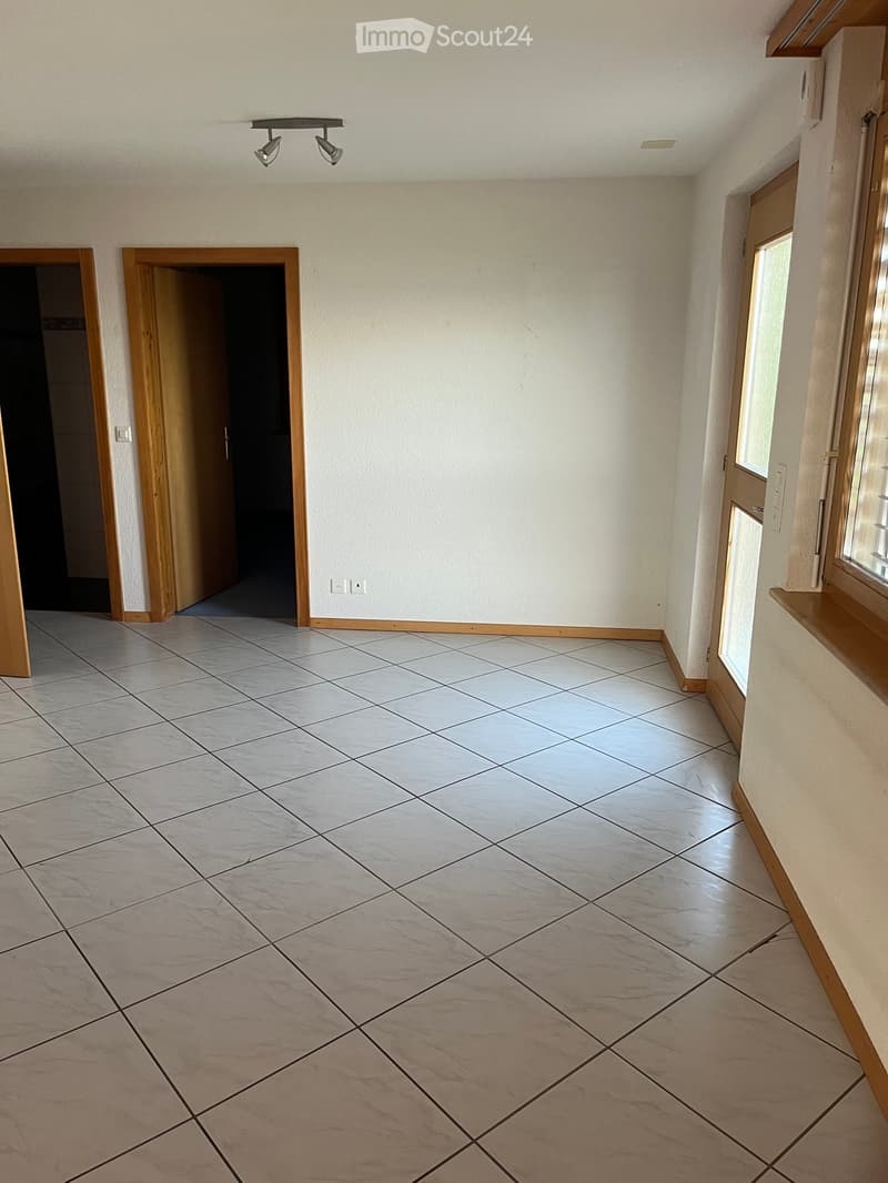 Empty room with tiled floor, white walls, and wooden trim around doors and windows. Features two doors and a window with blinds.