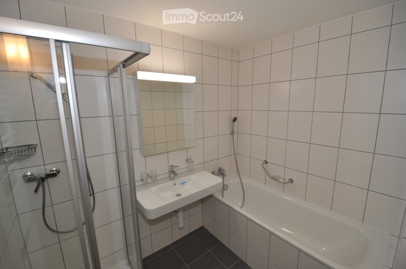 Modern white tiled bathroom with glass walk-in shower, bathtub, sink, and mirror.
