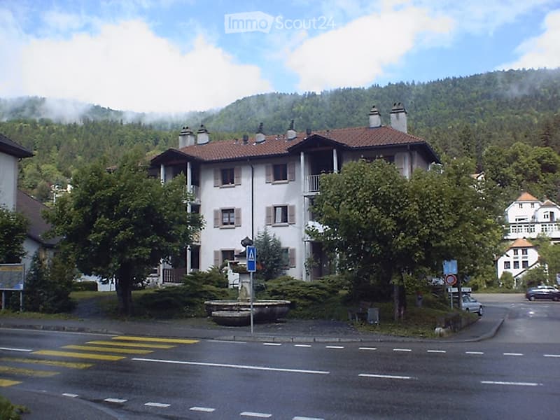 Multi-story residential building, red roof, surrounded by greenery, mountains in the background