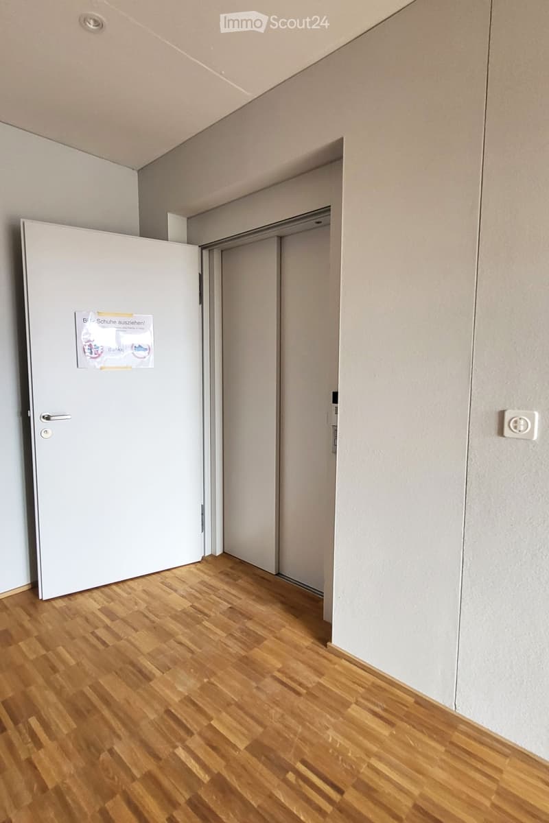 Empty room with white walls, wooden floor, white door, elevator door