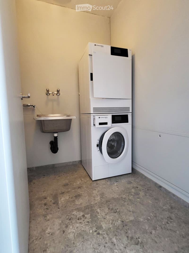 A small room with a white washing machine, a sink, and a faucet.