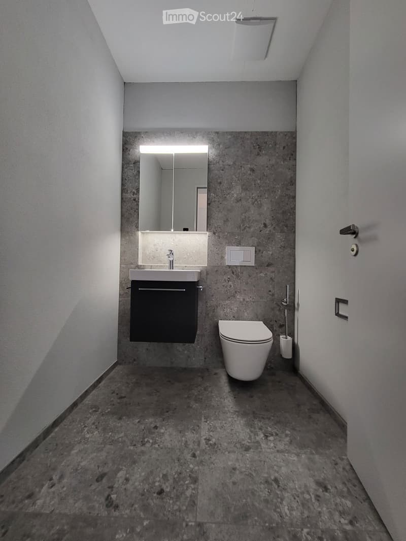 modern bathroom with white toilet, sink, mirror, and gray tiles