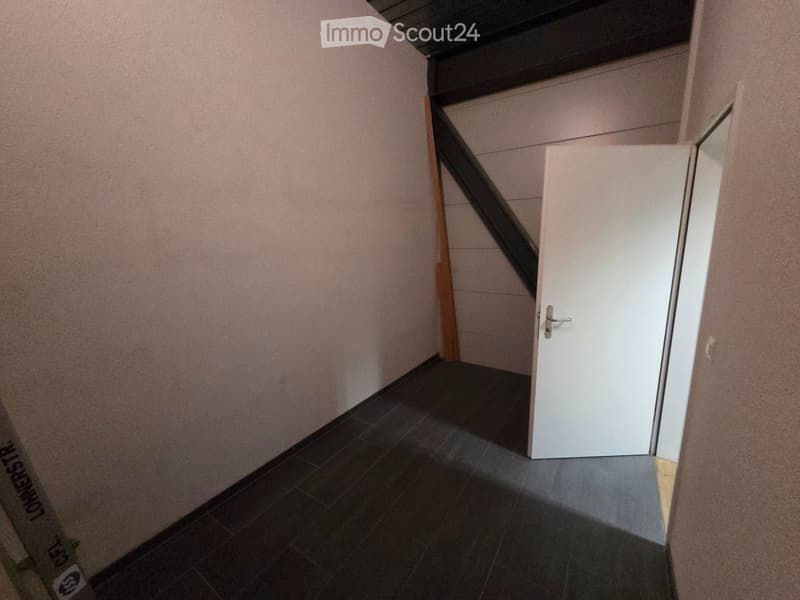 Empty room with white walls, black tiled floor, wooden beam, open door