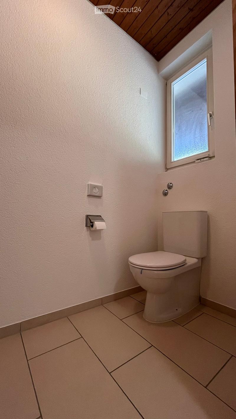 A small bathroom with white walls, tiled floor, a toilet, and a small window.