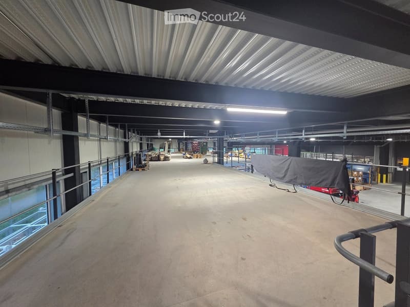 Empty warehouse with metal ceiling, metal railings, and large windows